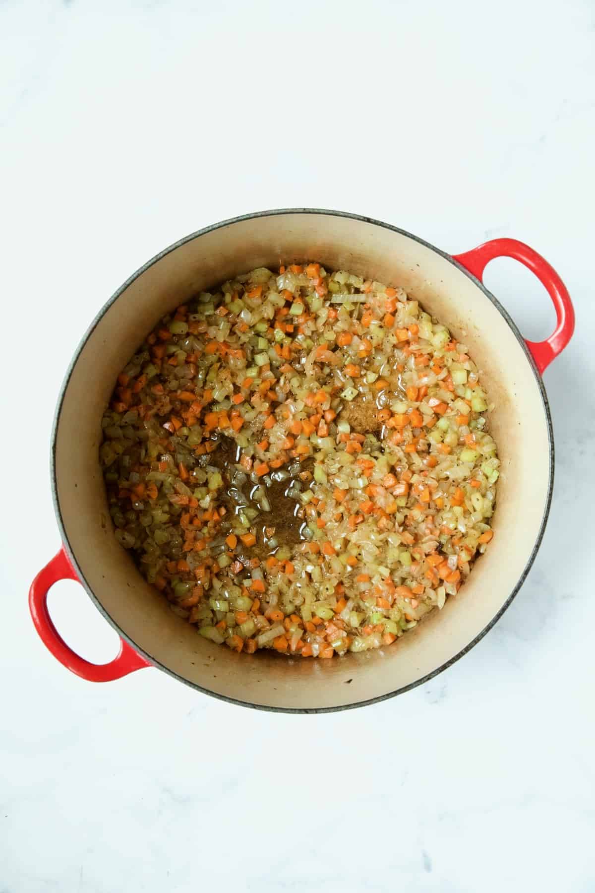 Cooked onions, celery and carrots in red enamel Dutch oven.