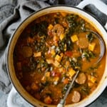 Chorizo Sweet Potato Stew with Kale in white Dutch oven with soup ladle.