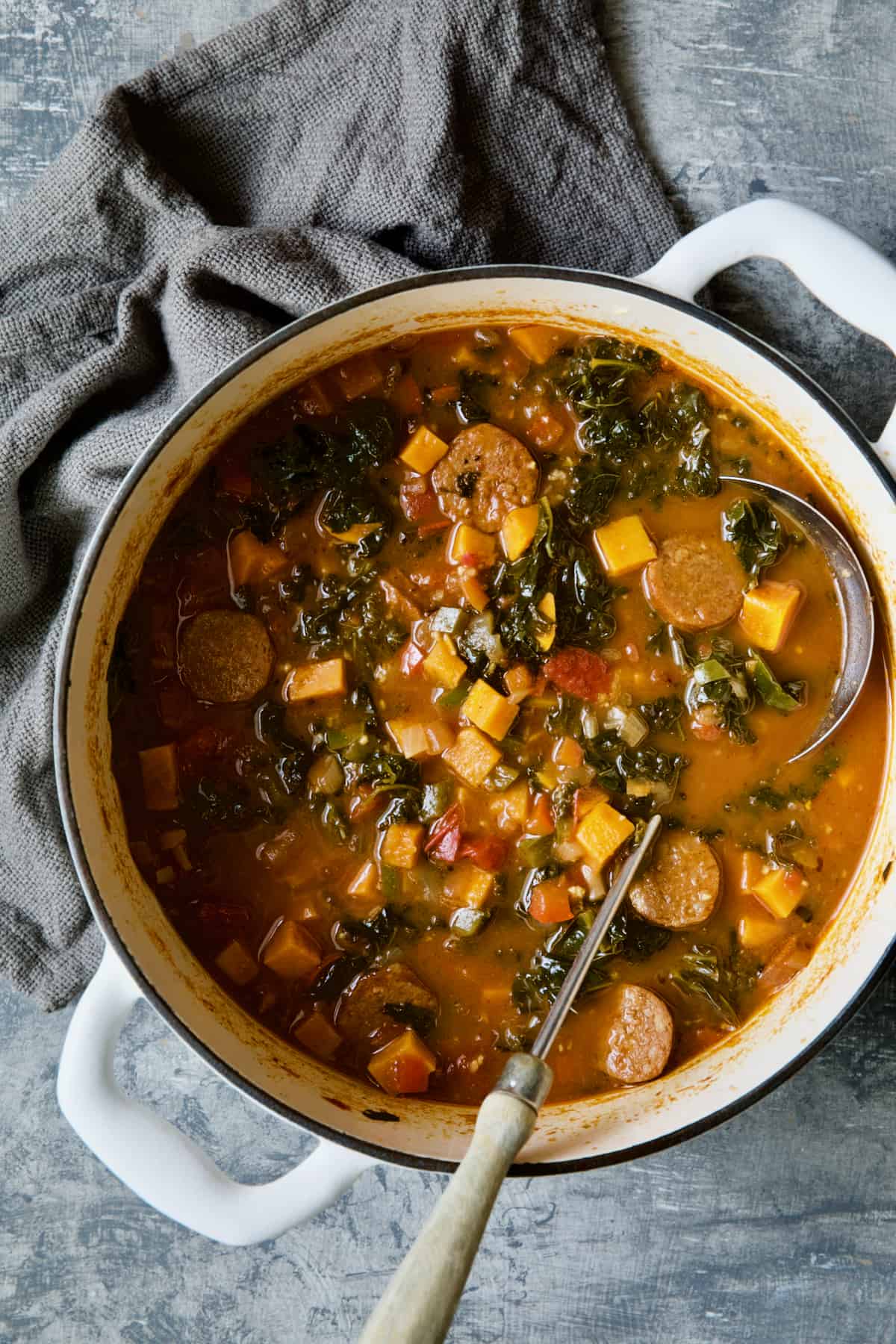 Chorizo Sweet Potato Stew with Kale in white Dutch oven with soup ladle.