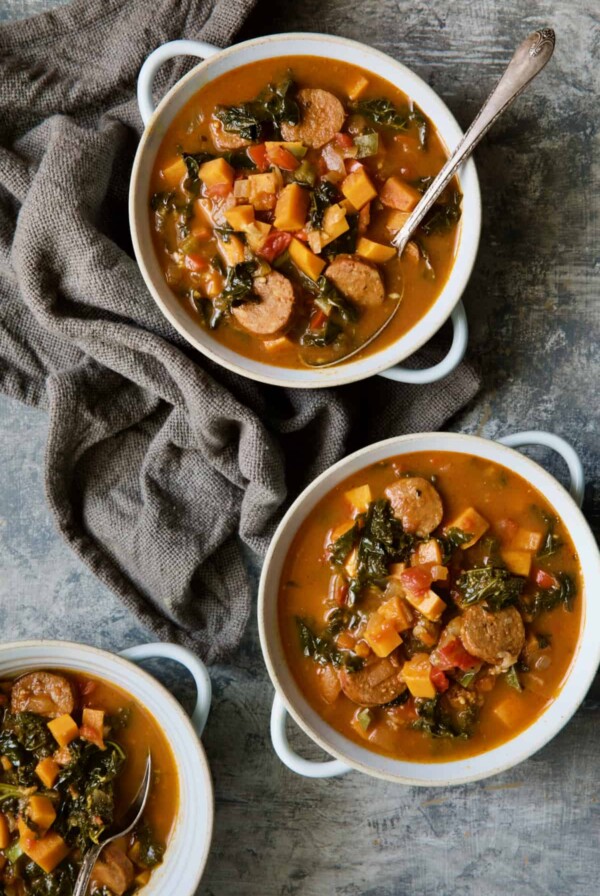 Chorizo Sweet Potato Stew with Kale in white bowls with soup spoon on gray background.