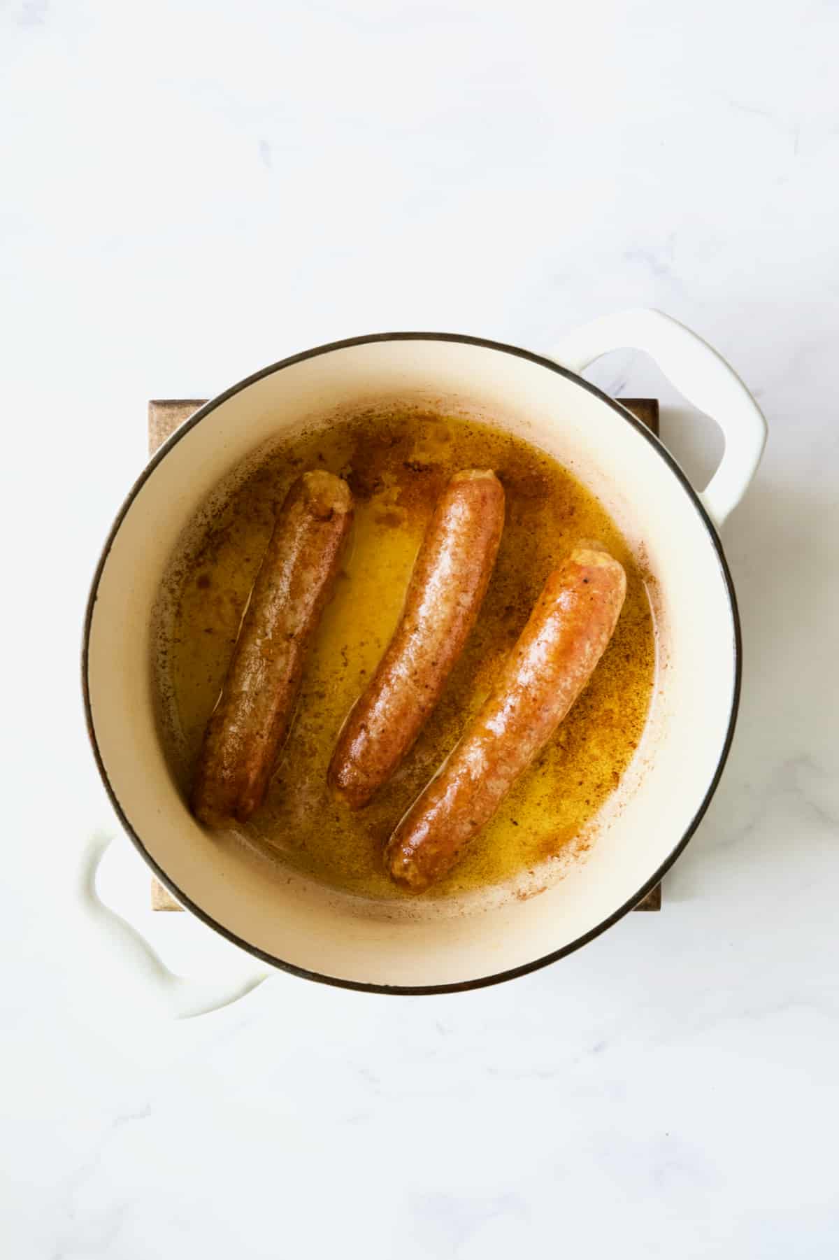 Three cooked chorizo links in white Dutch oven.