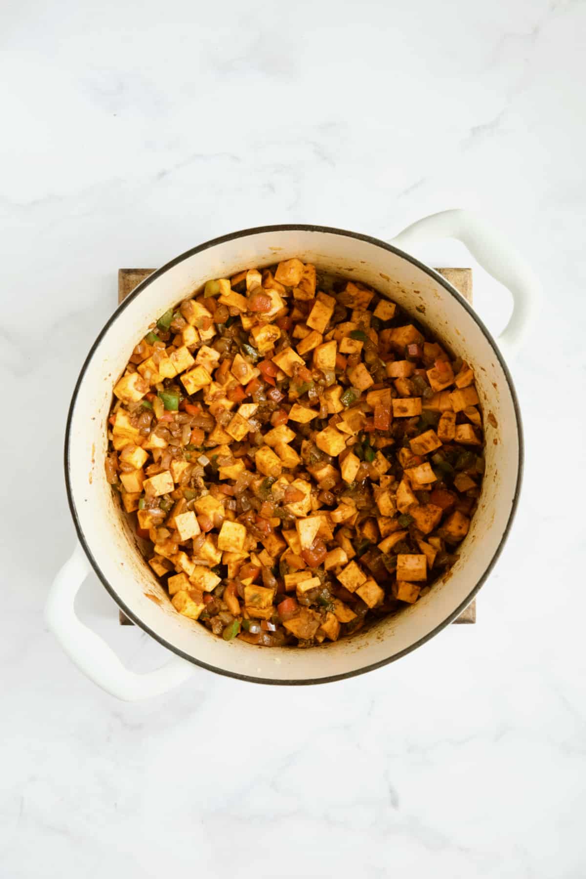 Sweet potatoes added to vegetables being cooked in white Dutch oven.