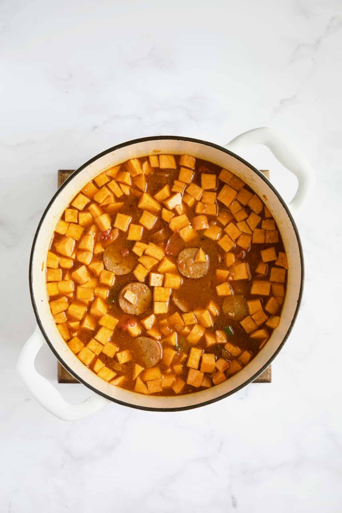 Sweet potatoes and chorizo added to stew in white Dutch oven.
