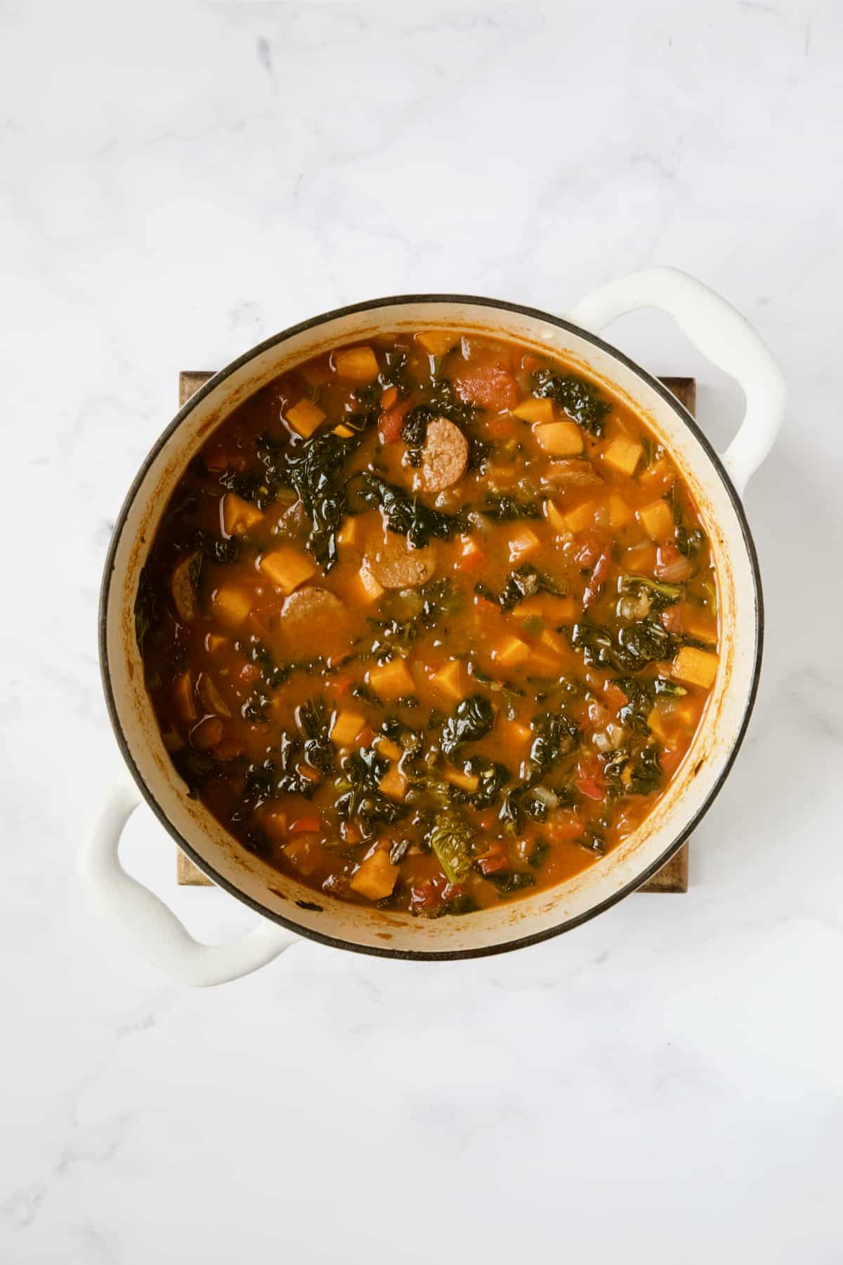 Finished Chorizo Sweet Potato Stew with Kale in white Dutch oven.
