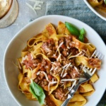 Slow Cooker Spicy Italian Sausage Ragu over pappardelle in white bowl garnished with fresh basil.