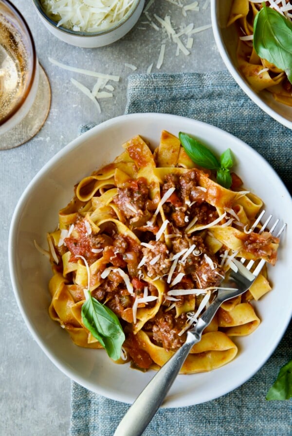 Slow Cooker Spicy Italian Sausage Ragu over pappardelle in white bowl garnished with fresh basil.