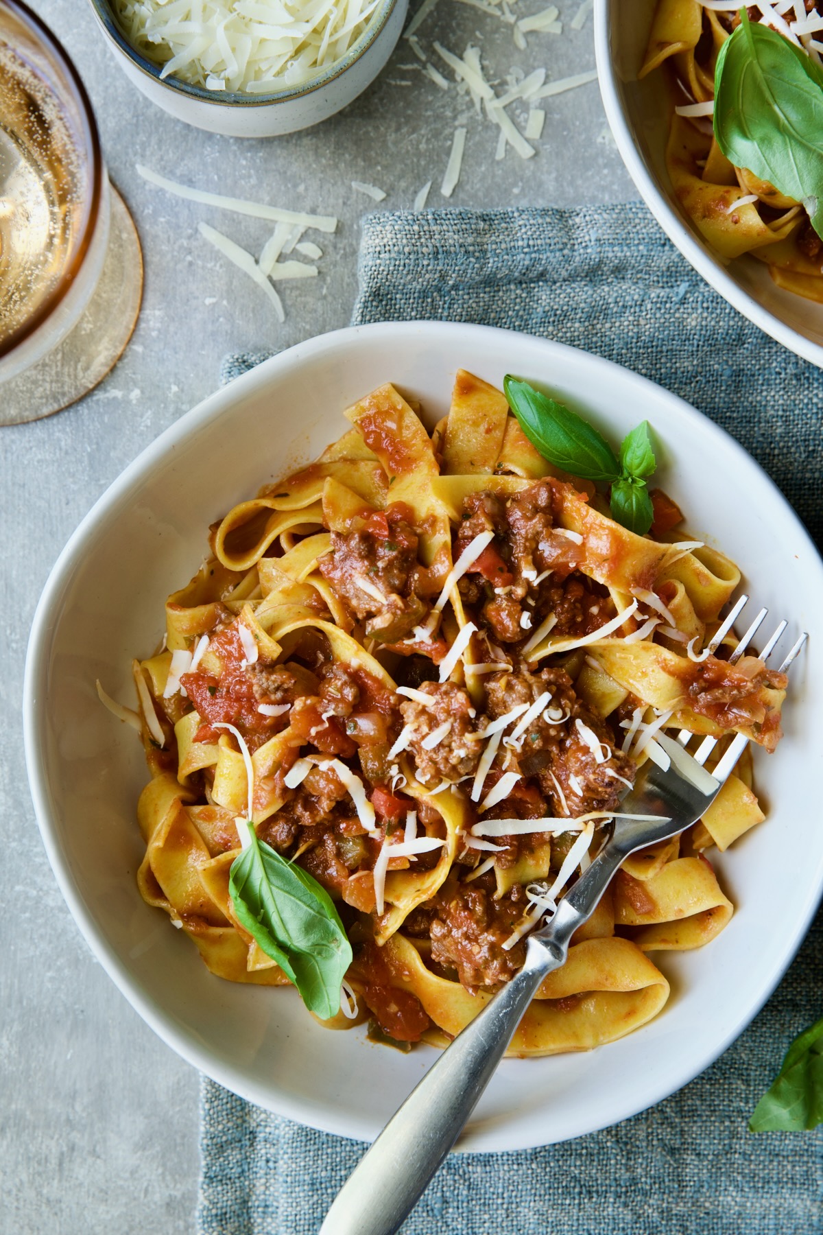 Slow Cooker Spicy Sausage and Pepper Ragu over pappardelle in white bowl garnished with fresh basil.