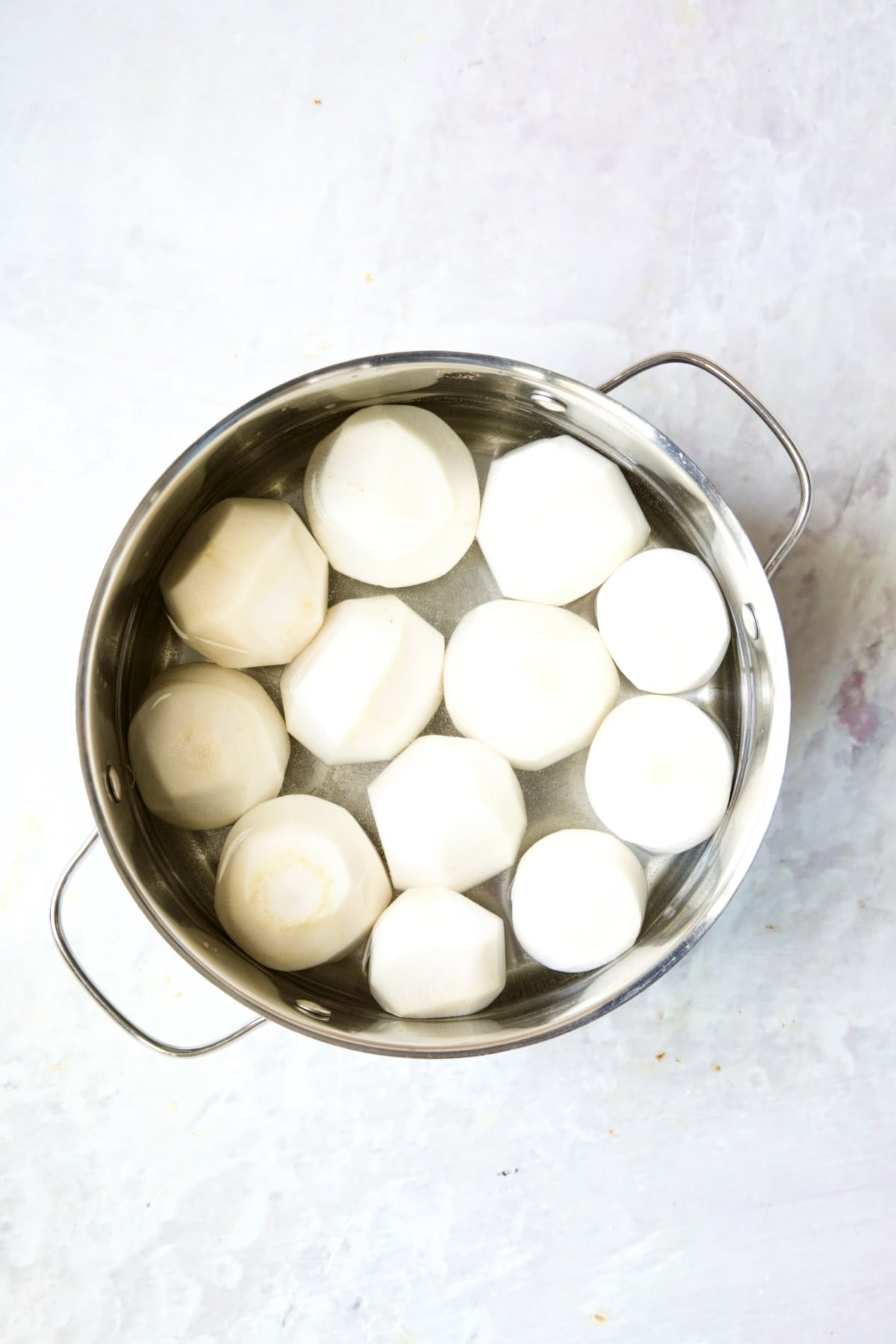 Uncooked turnips in stainless steel pot covered with water.