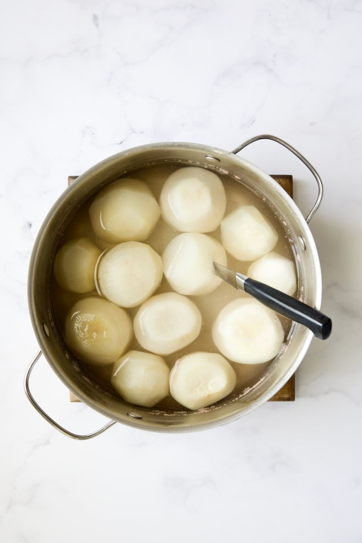 Cooked turnips in stainless steel pot with one pierced with a paring knife.