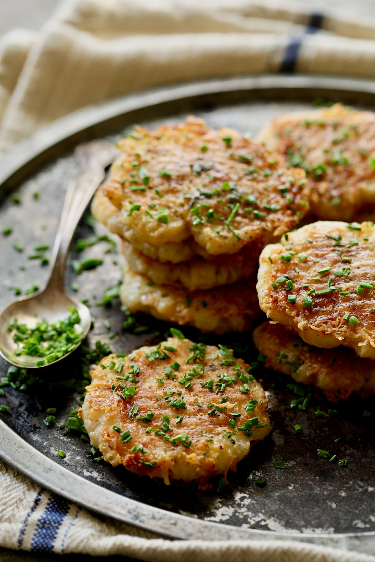 Parmesan Crusted Crushed Turnips on stainless steel tray with spoon full of chives spilling over.