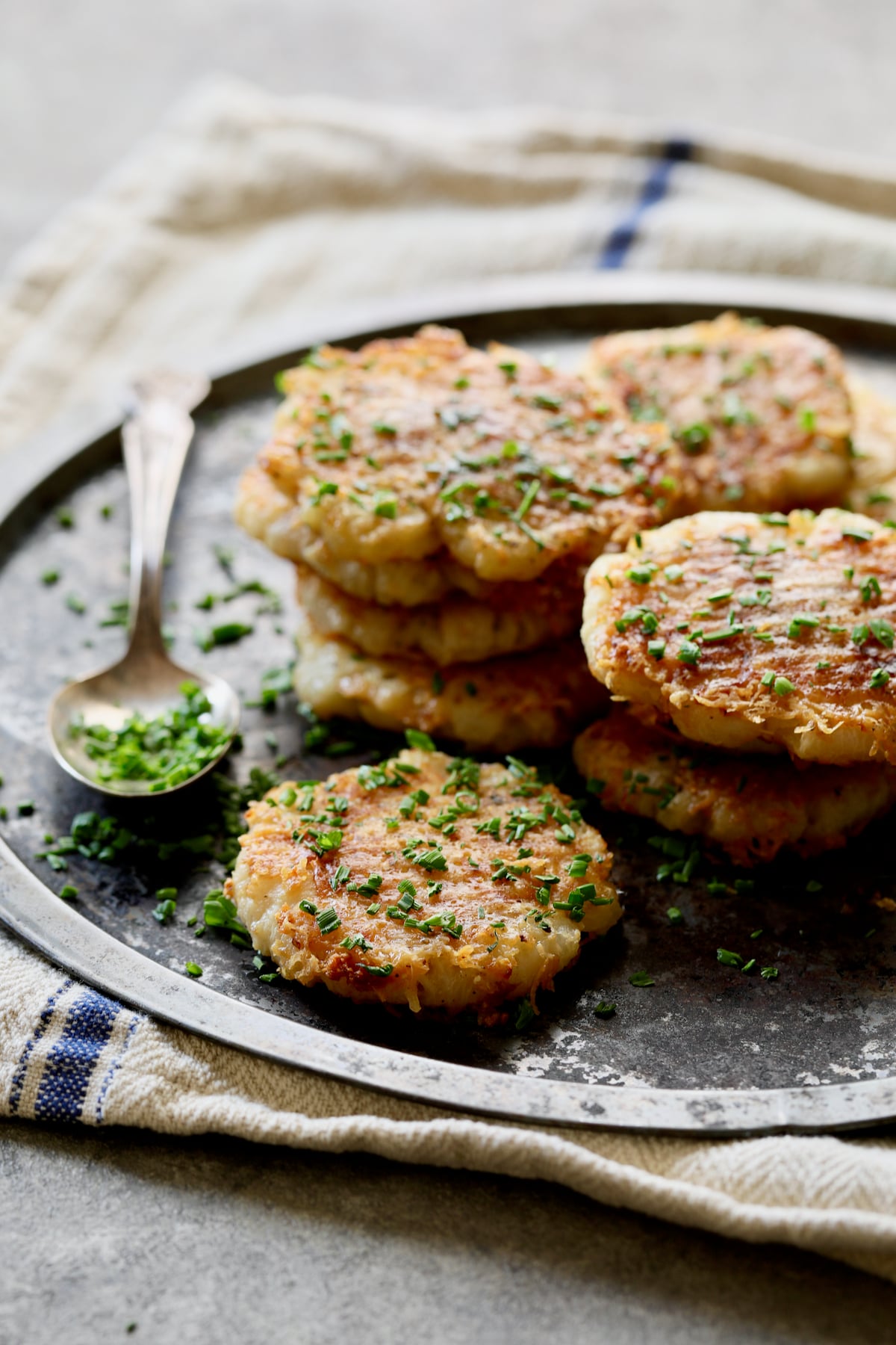 Stacked Parmesan Crusted Crushed Turnips on stainless steel tray garnished with chopped fresh chives.
