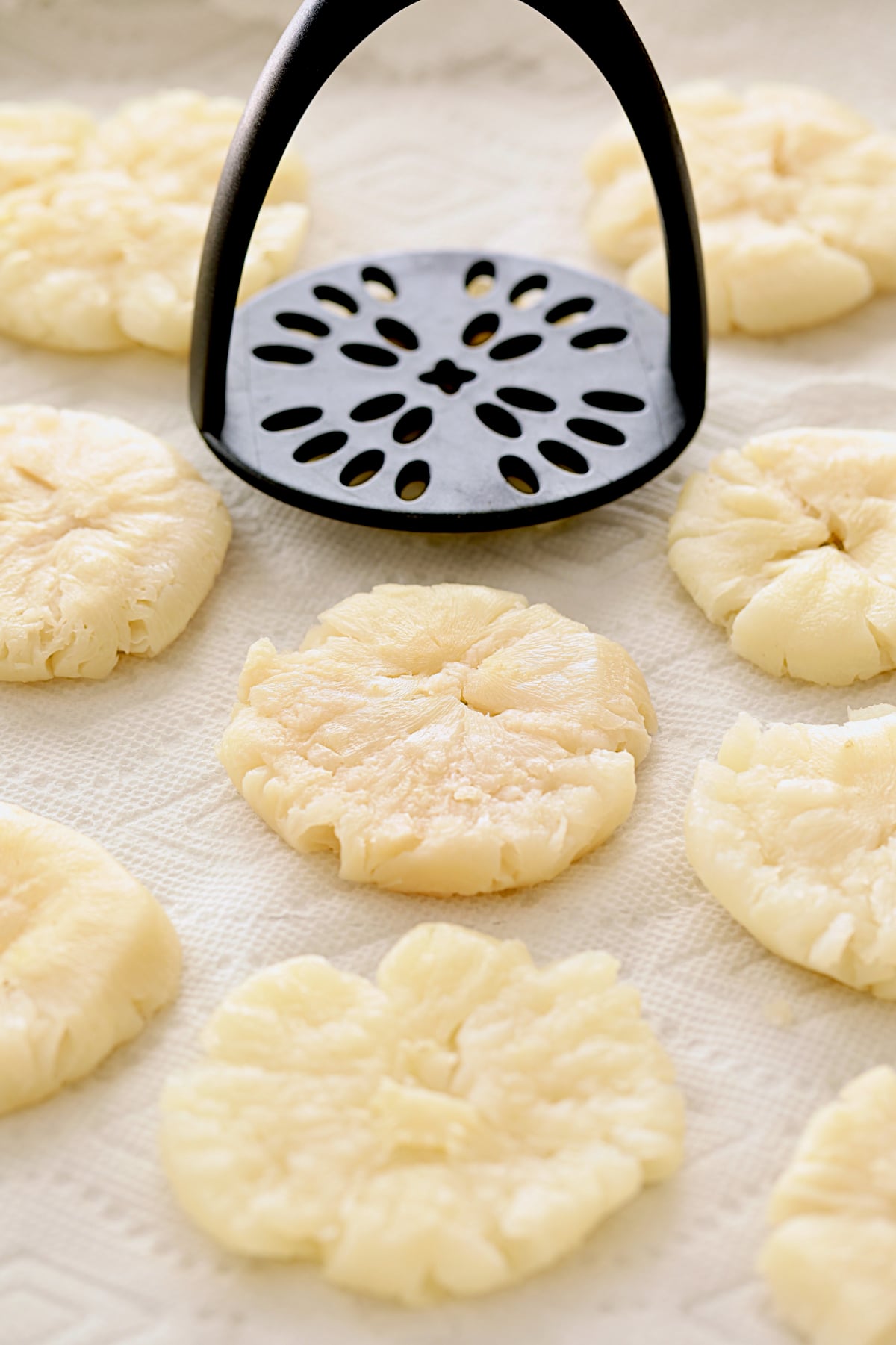 Cooked turnips on paper towels being smashed with potato masher.