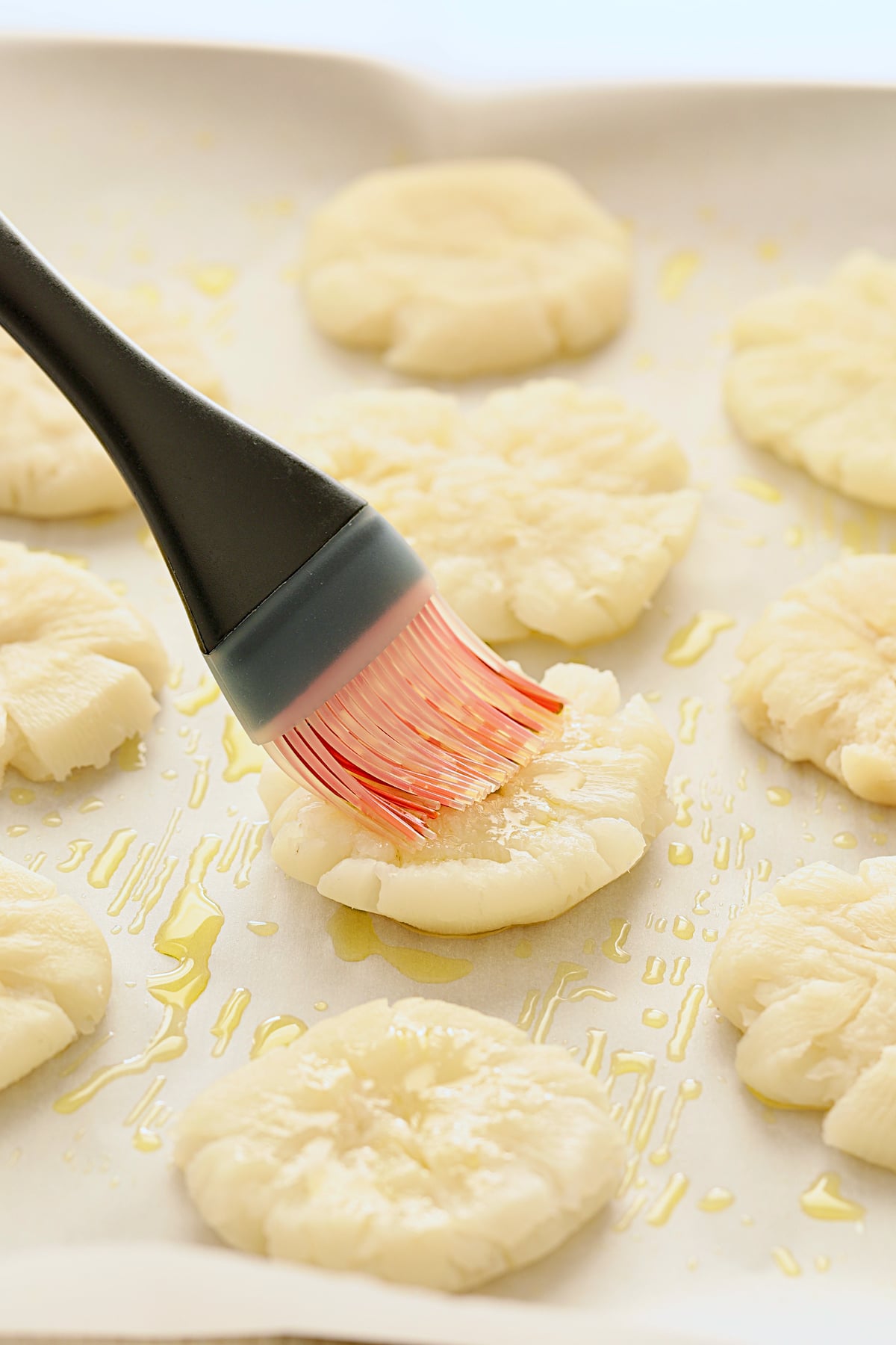 Smashed turnips on parchment paper being brushed with olive oil.