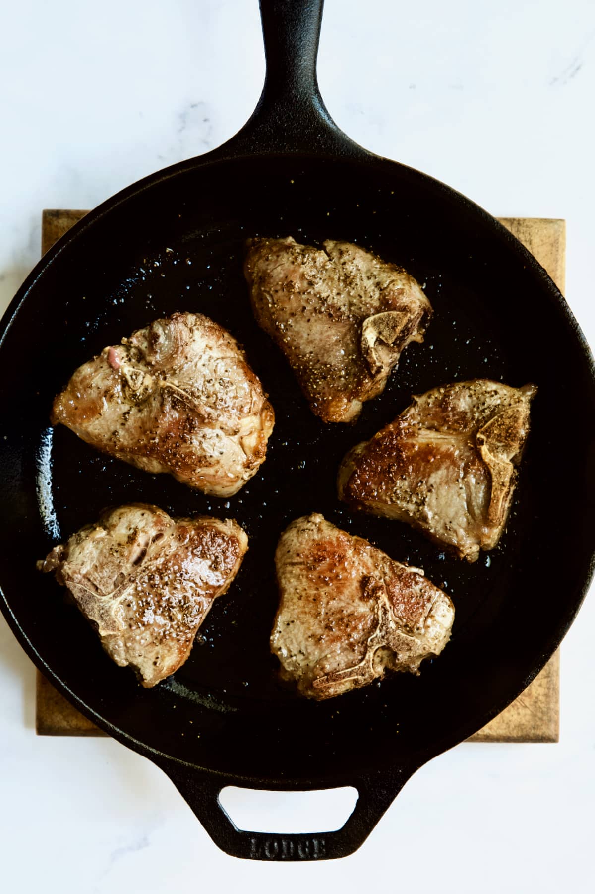 Five seared lamb chops in cast iron skillet.