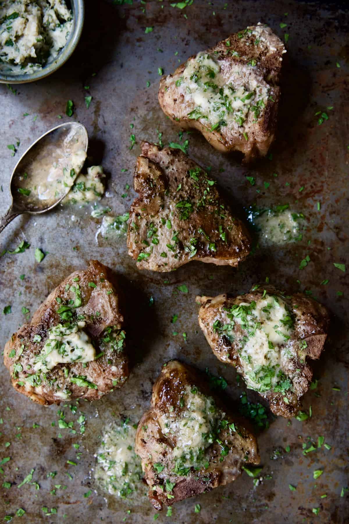 Seared Lamb Chops with Anchovy Butter on baking sheet with butter melting off spoon.