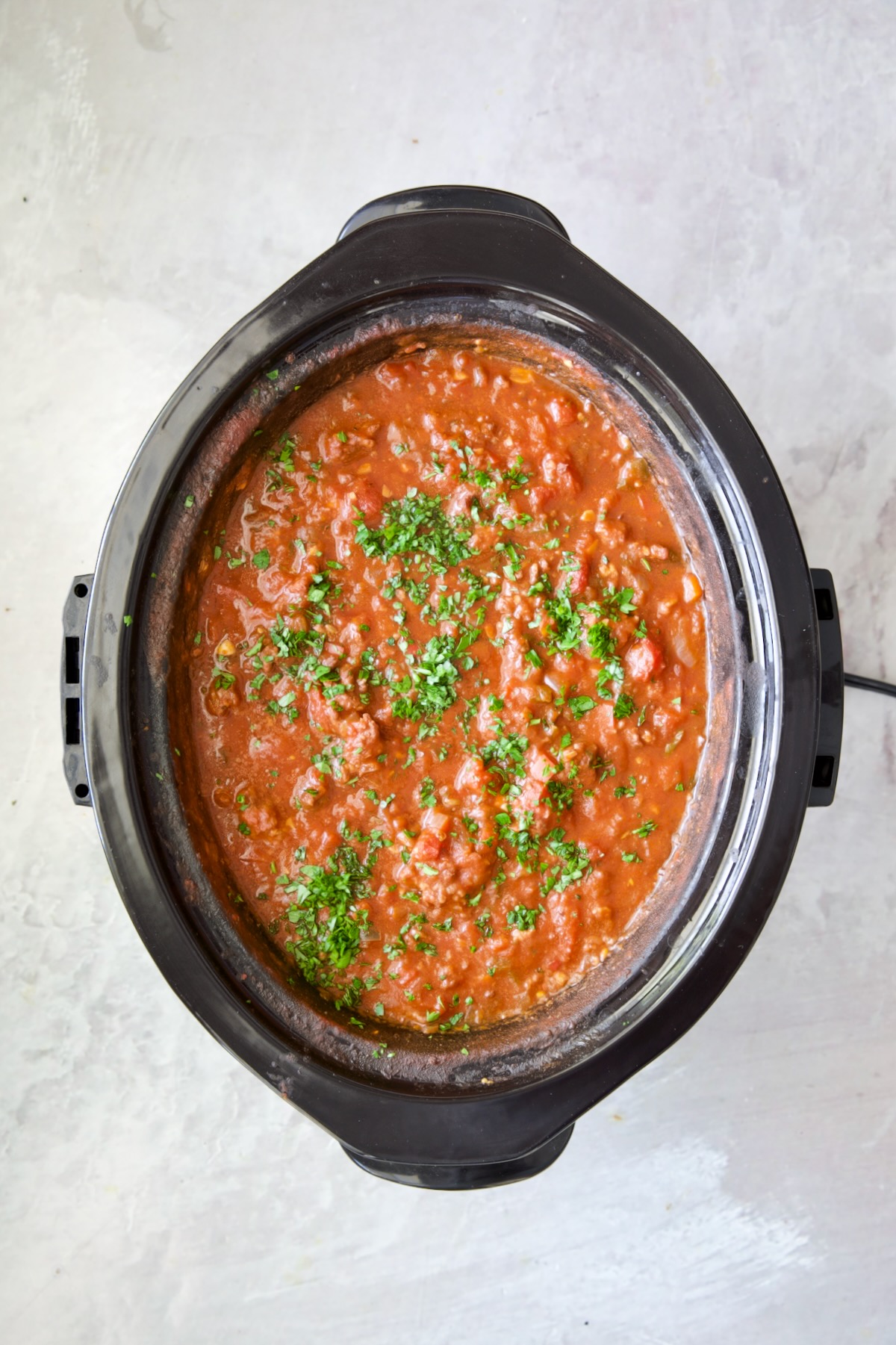 Slow Cooker Spicy Sausage and Pepper Ragu in slow cooker garnished with fresh parsley.