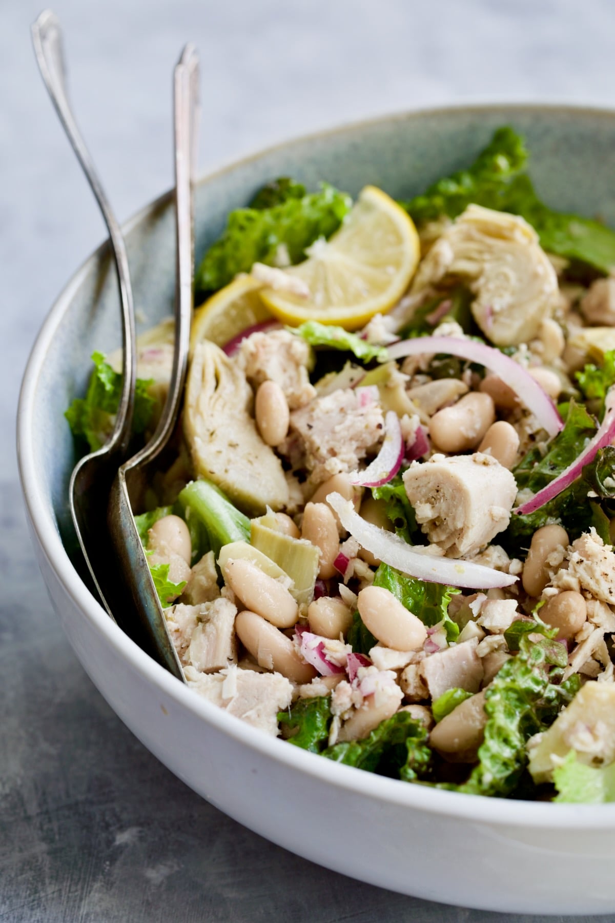 Salad in serving bowl with serving utensils.