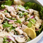 Finished salad in white serving bowl with silver serving utensils.