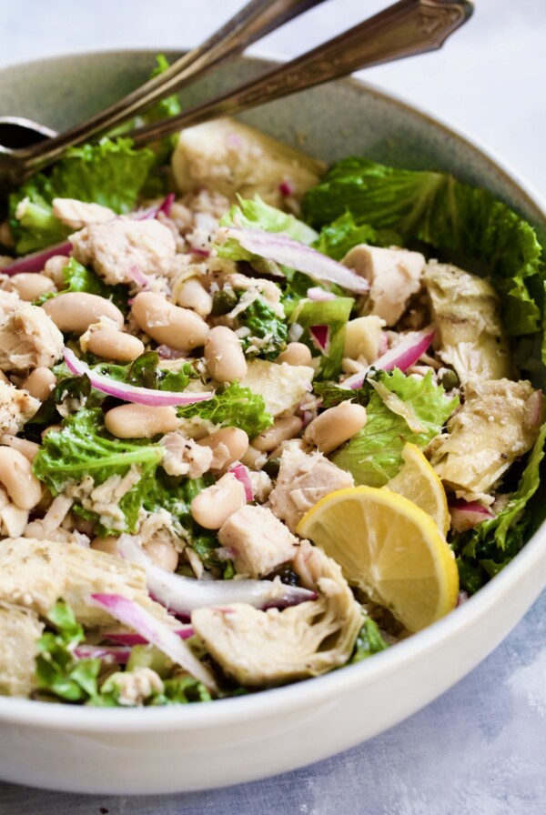Finished salad in white serving bowl with silver serving utensils.