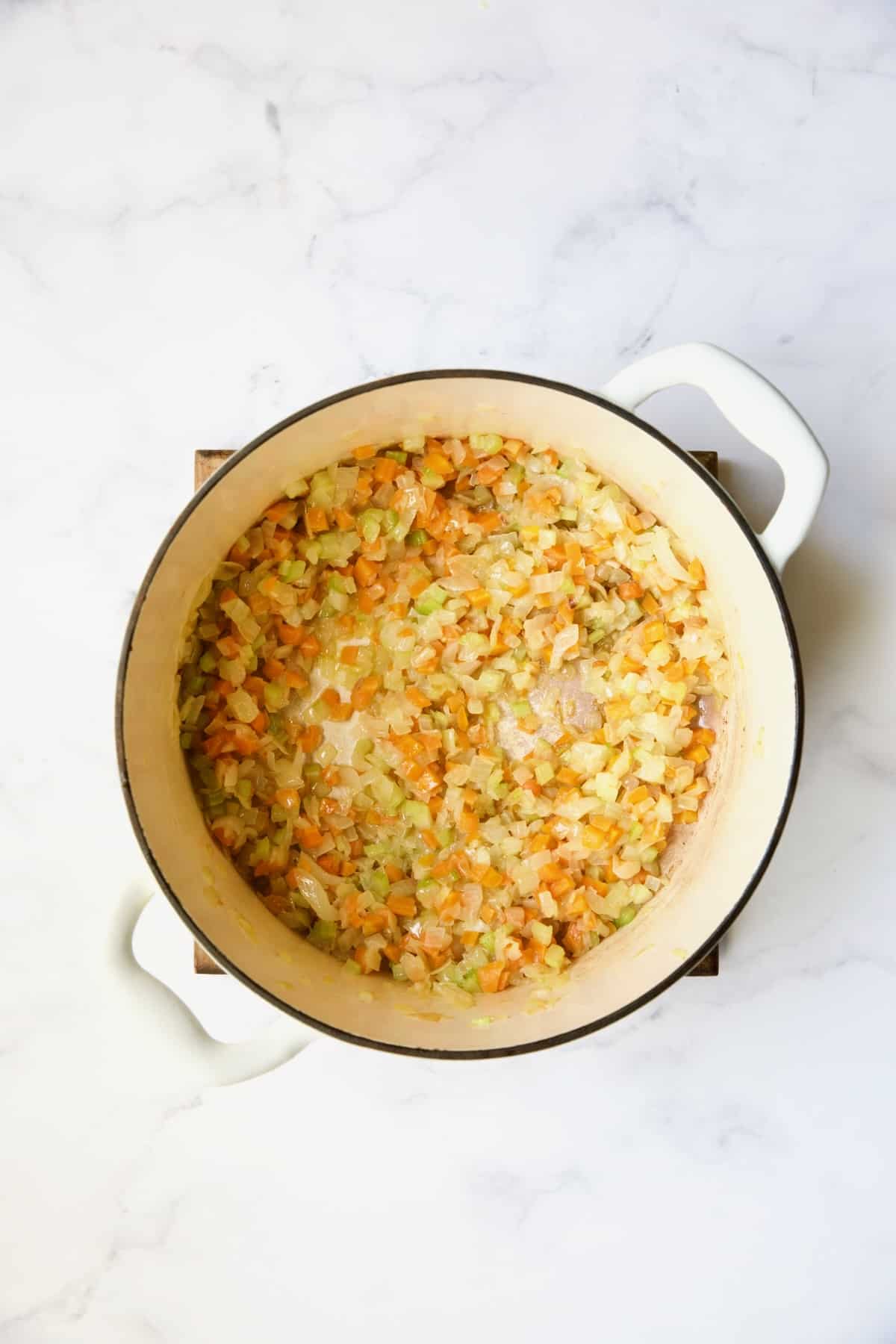 Cooked onions, celery and carrots in white Dutch oven.
