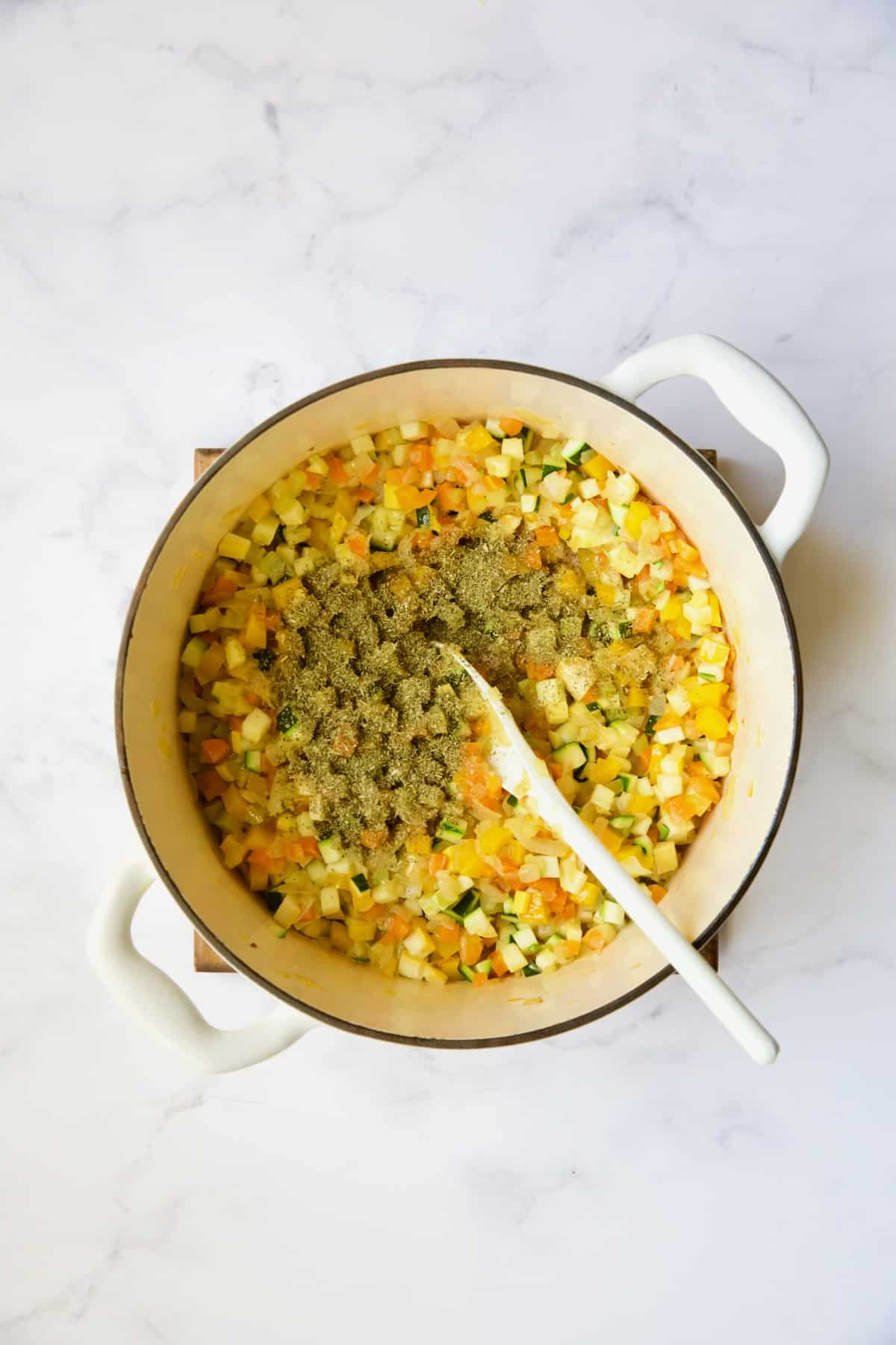 Cooked vegetables in white Dutch oven with Italian seasoning added about to be stirred.