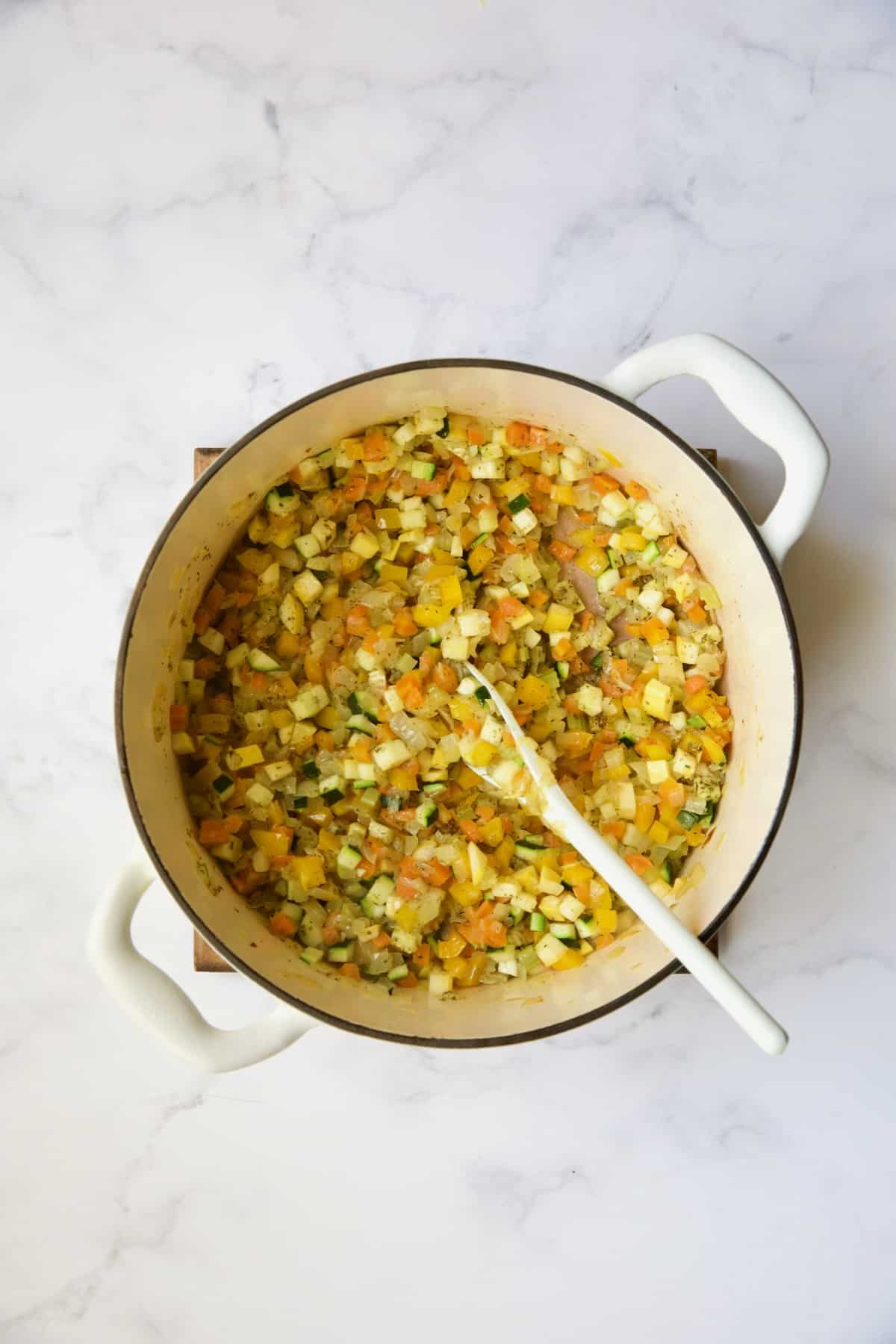 Cooked vegetables with Italian seasoning in white Dutch oven.