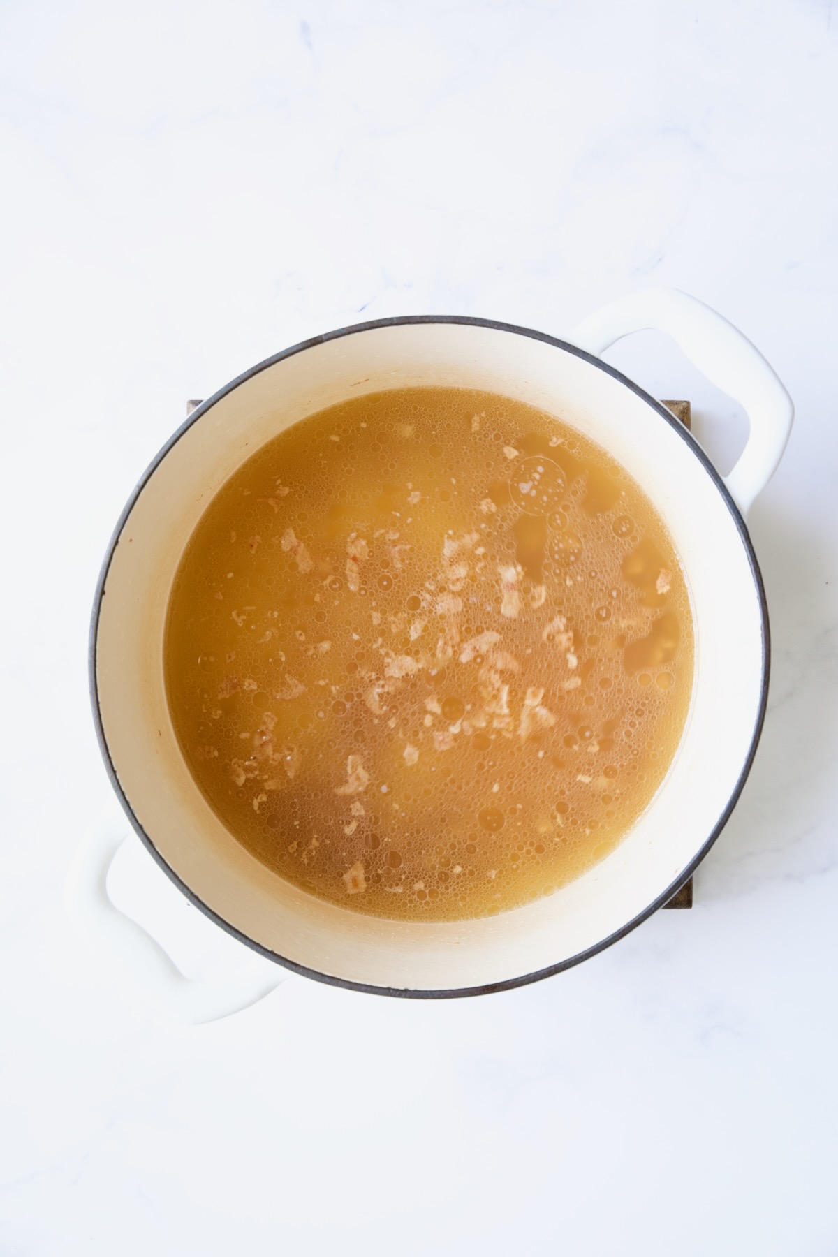 Chicken broth and bacon in white Dutch oven.
