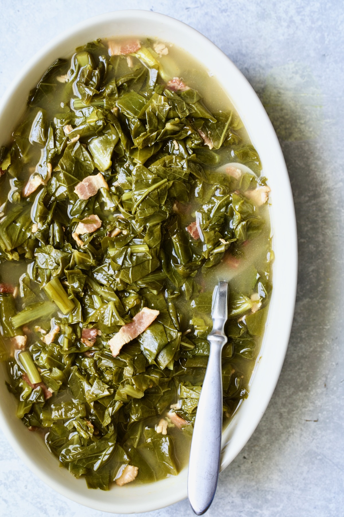 Braised Southern Greens in oval serving bowl with serving spoon.