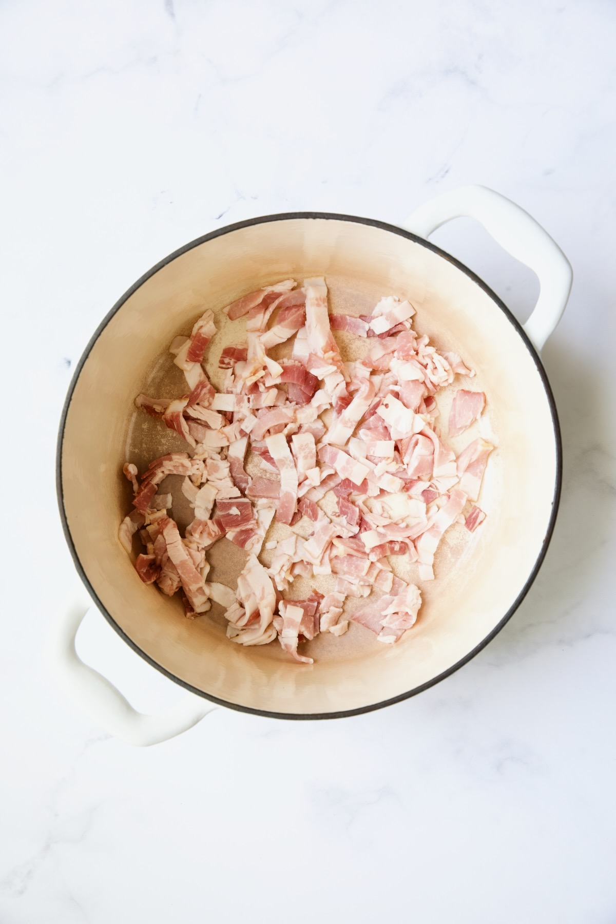 Uncooked bacon in white Dutch oven.