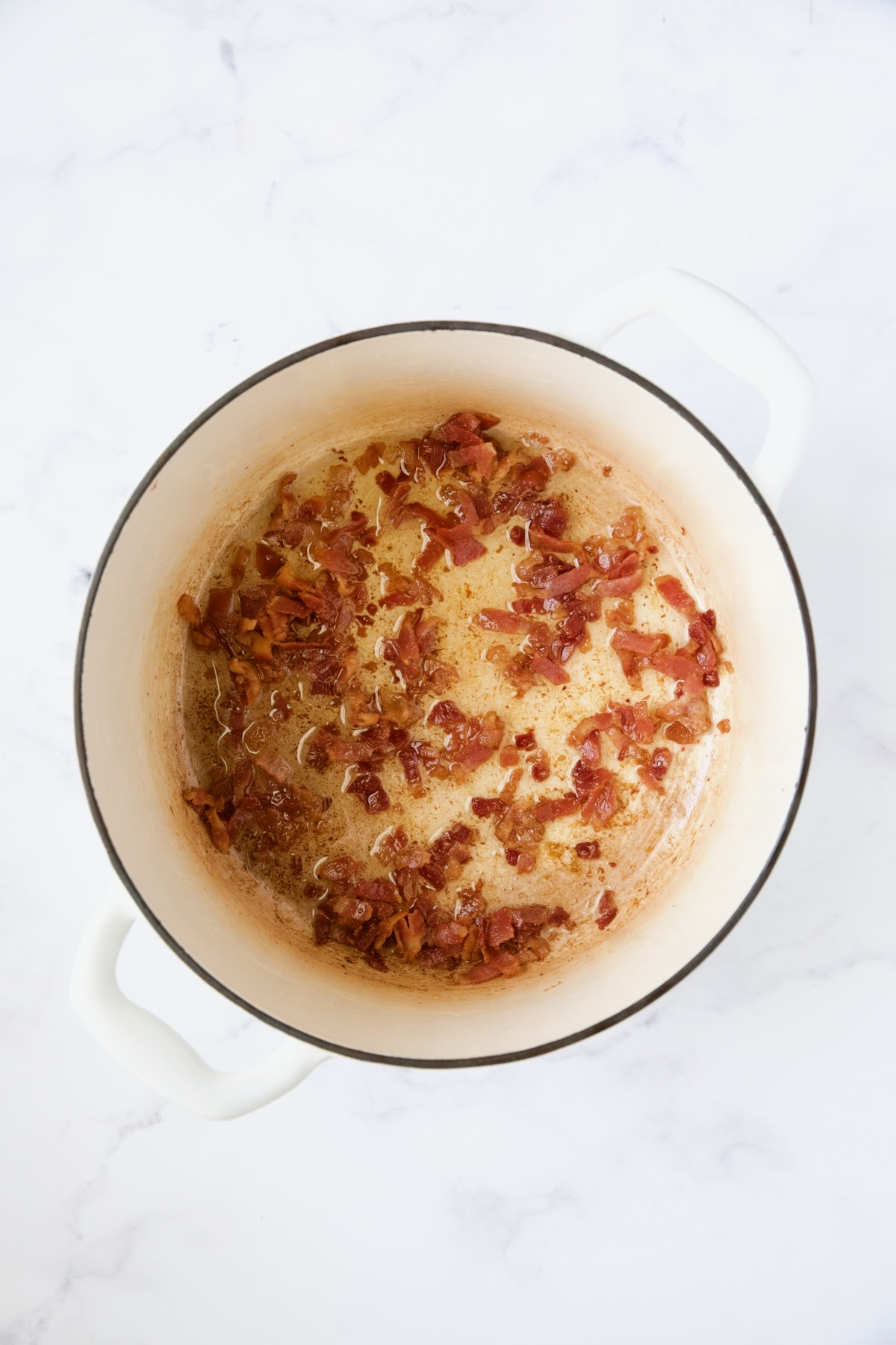 Cooked bacon in white Dutch oven.