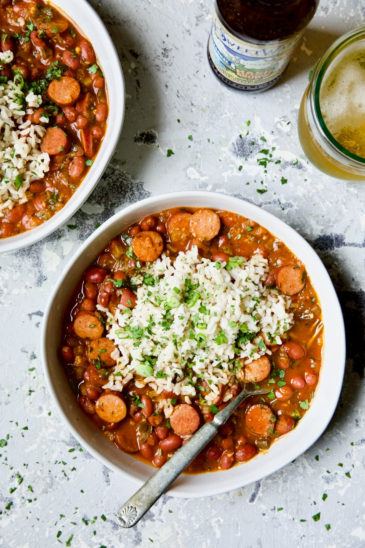 Two bowls of Easy Red Beans and Rice on light blue background with glass of beer and bottle.