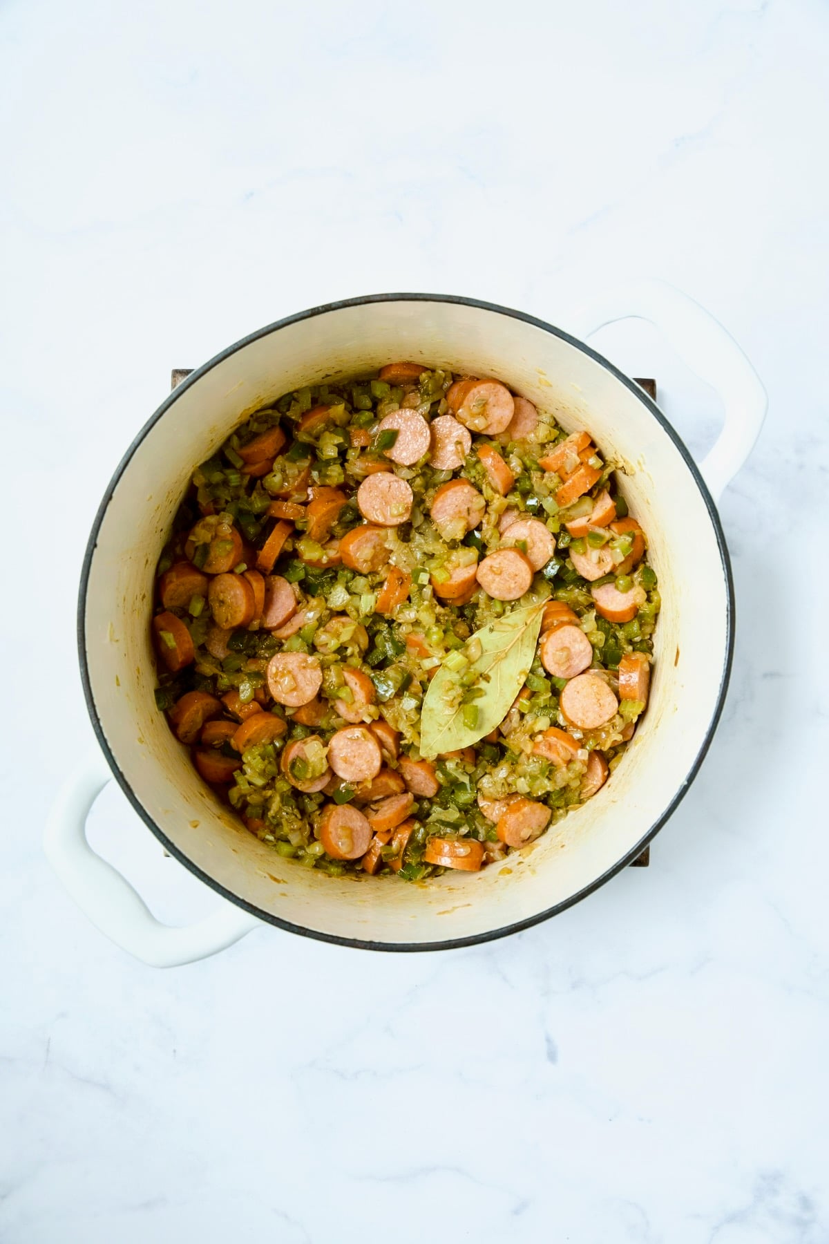 Onions, celery, green pepper and andouille sausage in white Dutch oven.