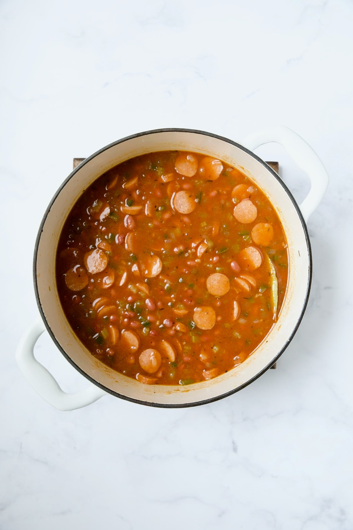 Beans and andouille sausage in white Dutch oven before being cooked.