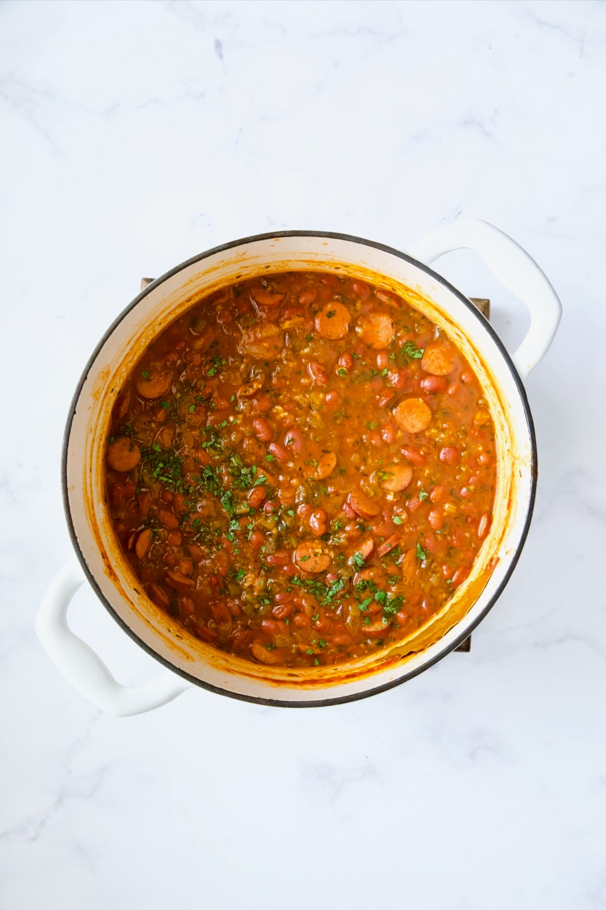 Red beans and andouille sausage in white Dutch oven after being cooked.