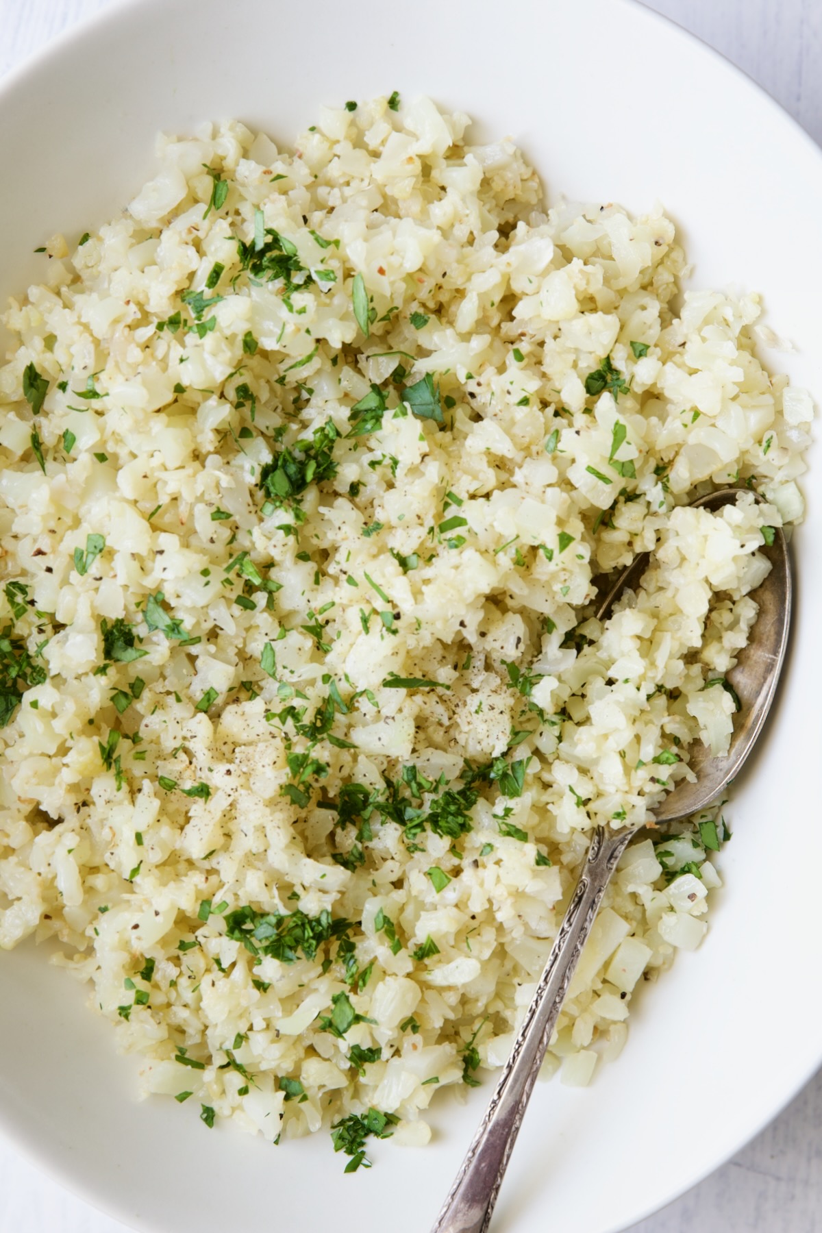 Photo of cauliflower rice in white oval bowl with serving spoon.