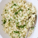 Cauliflower rice garnished with fresh parsley in white oval bowl.