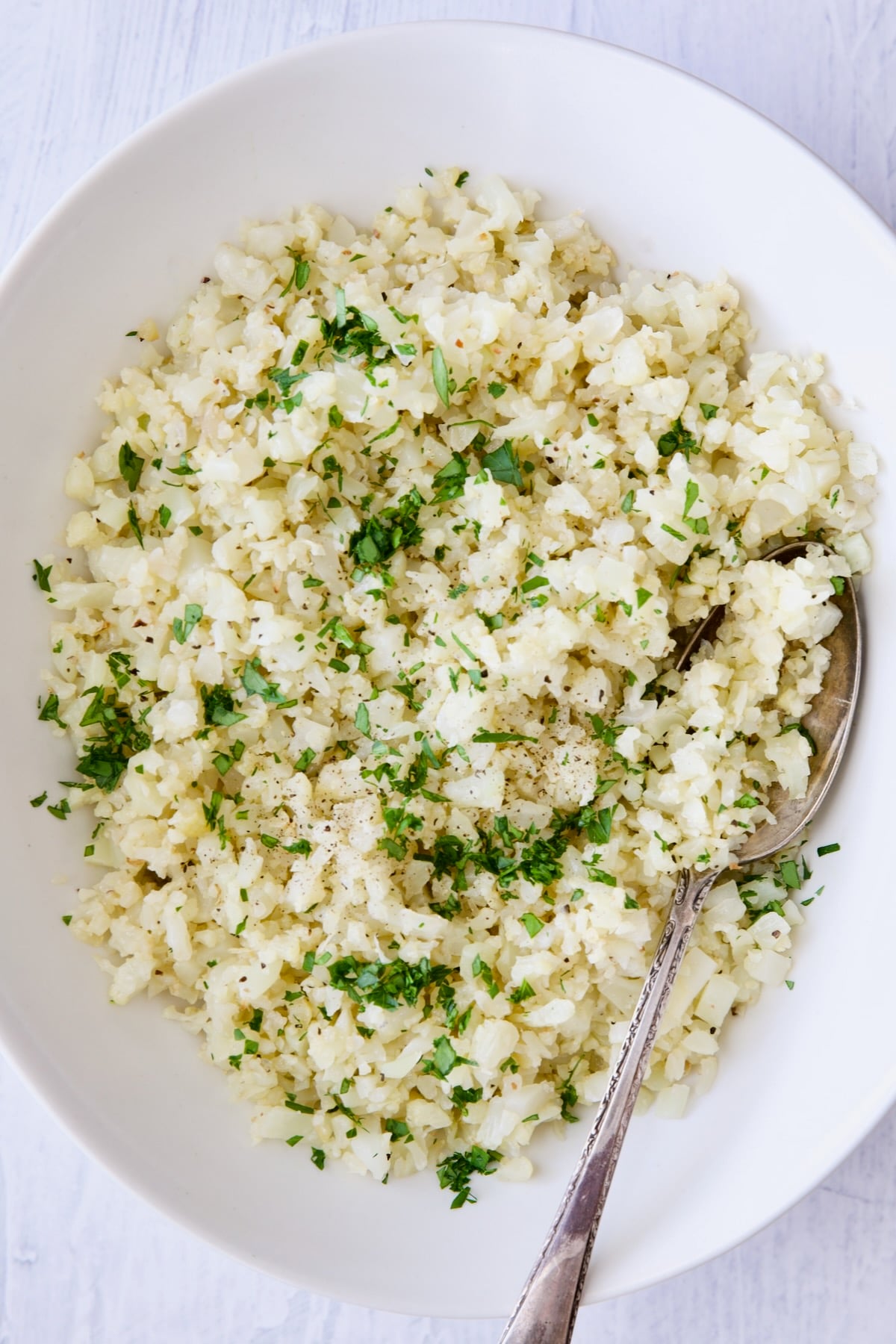 Cauliflower rice garnished with fresh parsley in white oval bowl.