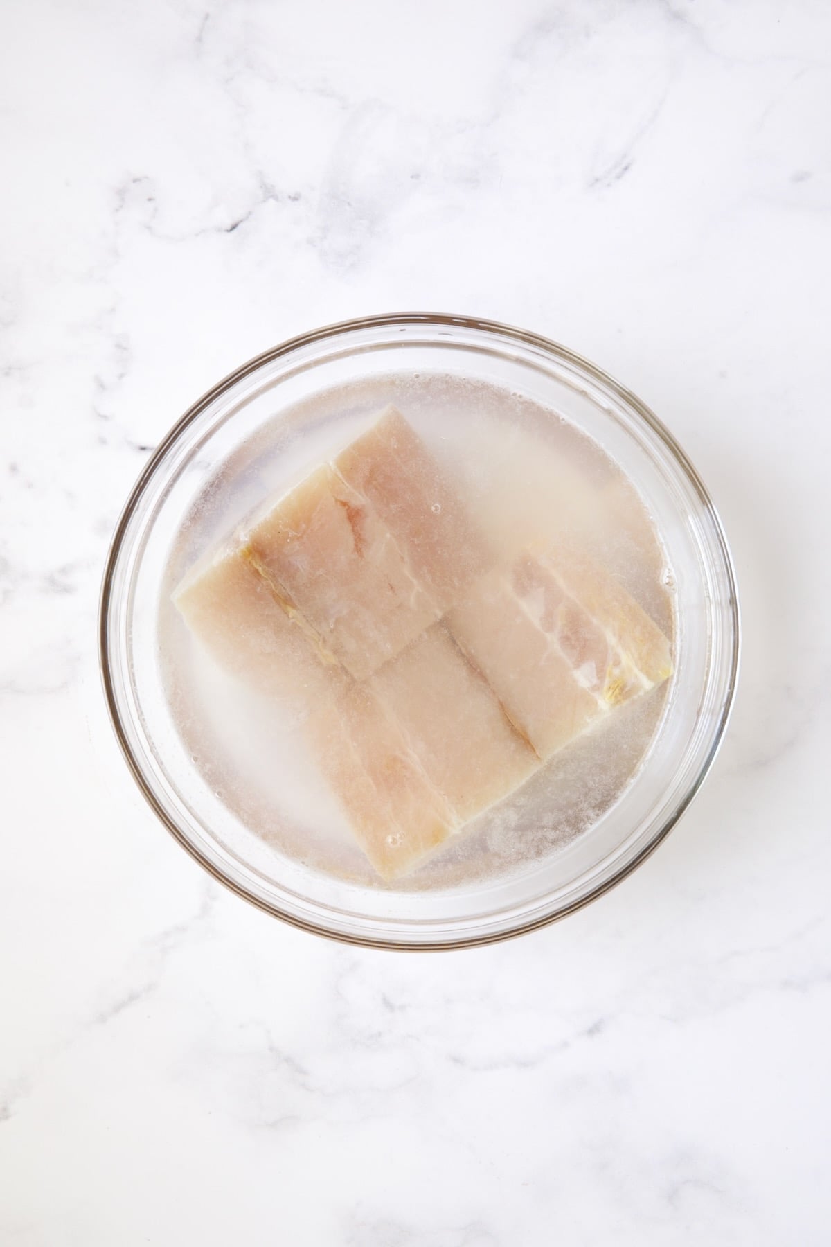 Two pieces of mahi-mahi in water in glass bowl.