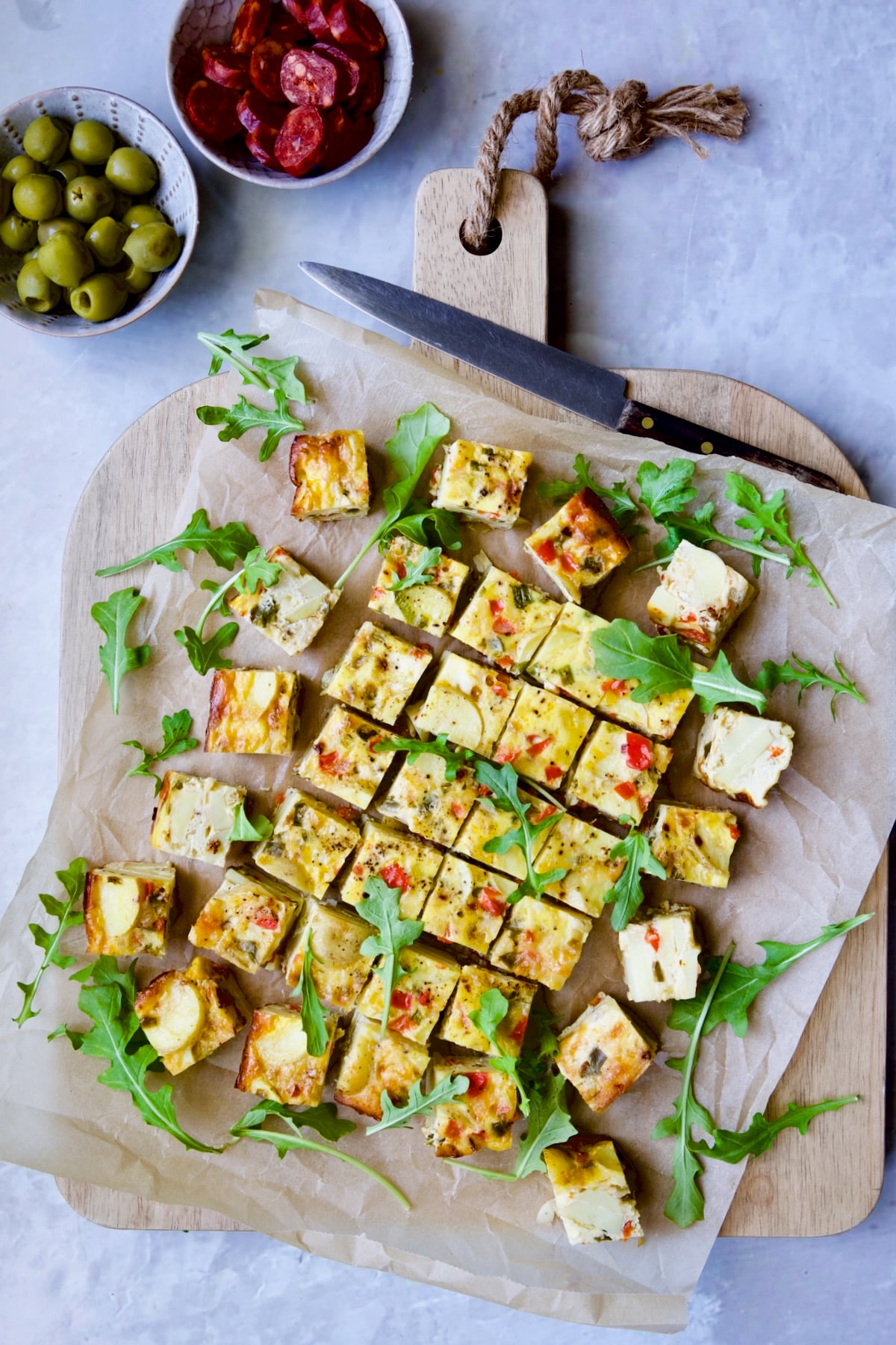 Oven-Baked Spanish Tortilla on parchment paper set on cutting board garnished with arugula.
