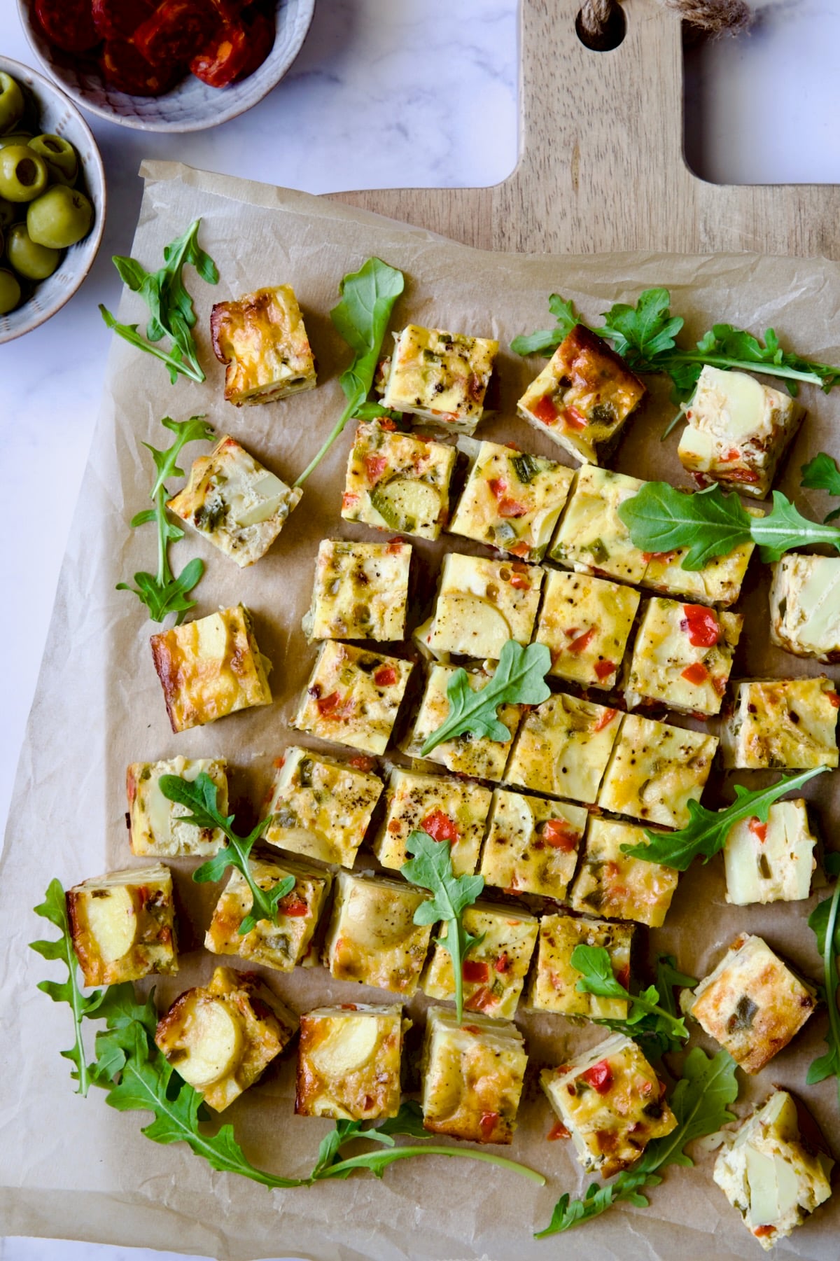 Oven-Baked Spanish Tortilla on parchment paper set on cutting board garnished with arugula.