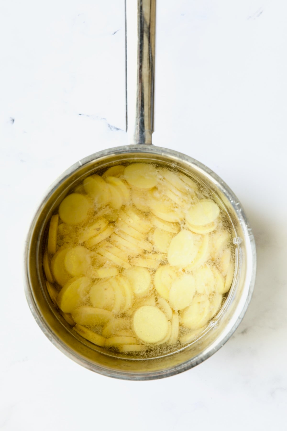 Cooked potato slices in saucepan.