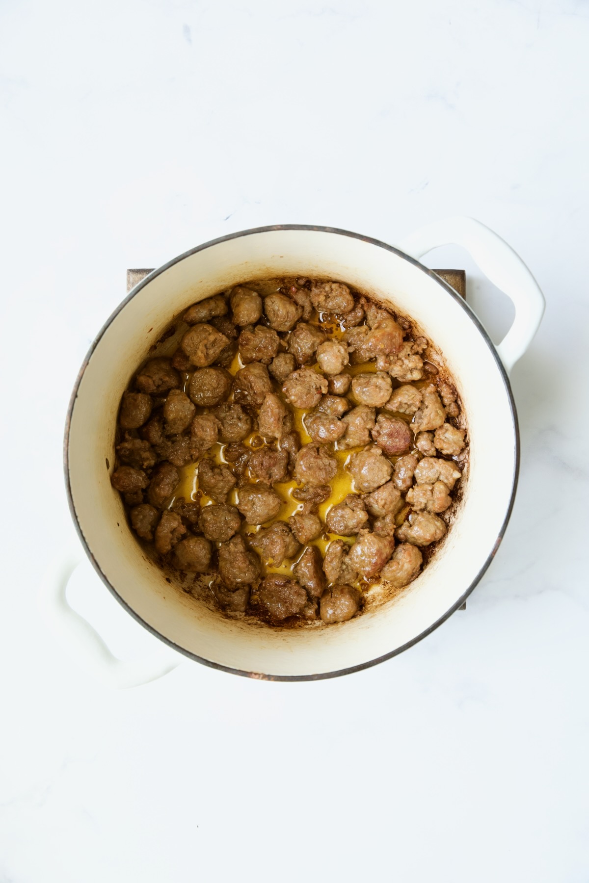Cooked Italian sausage in white Dutch oven.