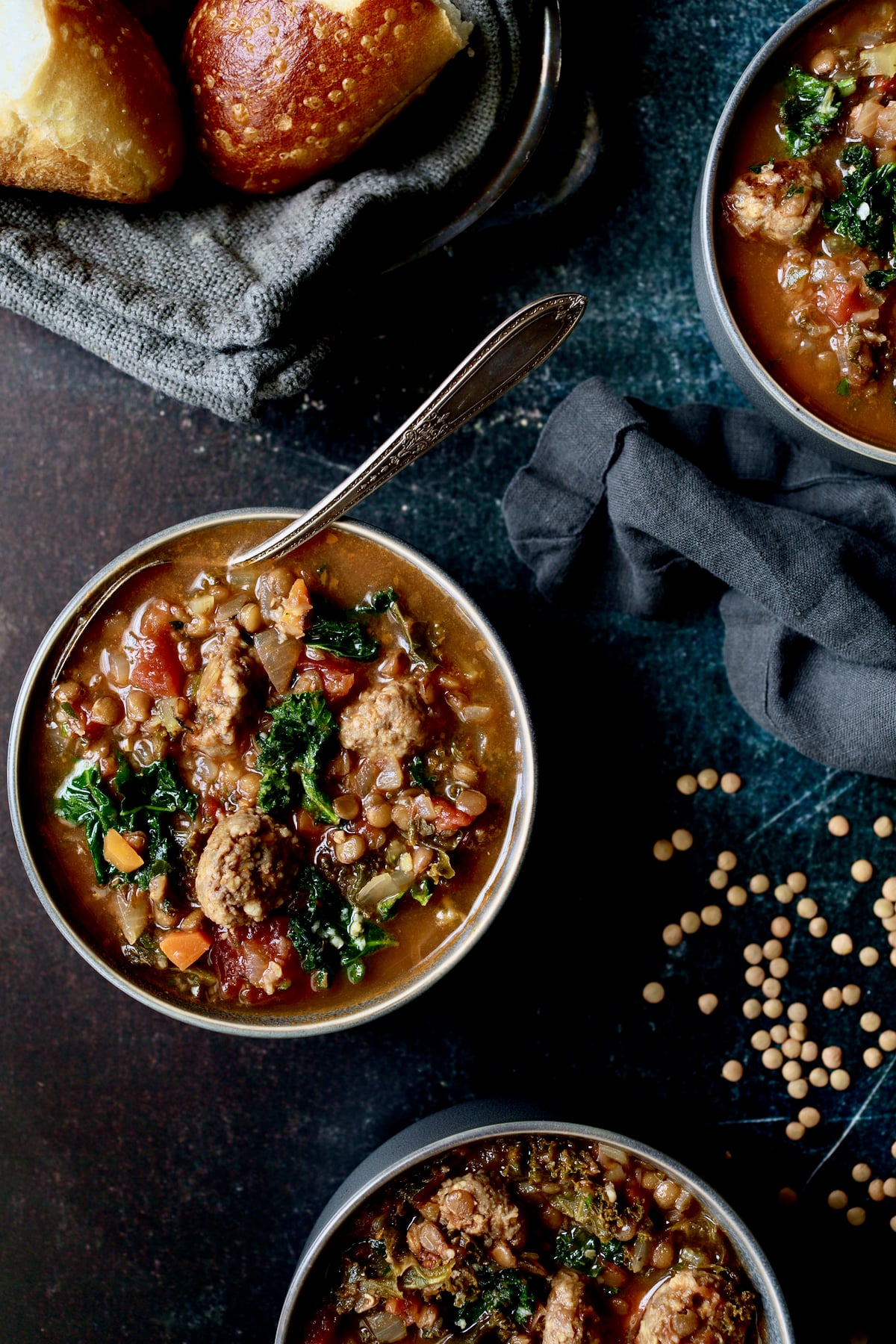 One bowl of Sausage and Lentil Soup with Kale with gray napkin and lentils scattered about.