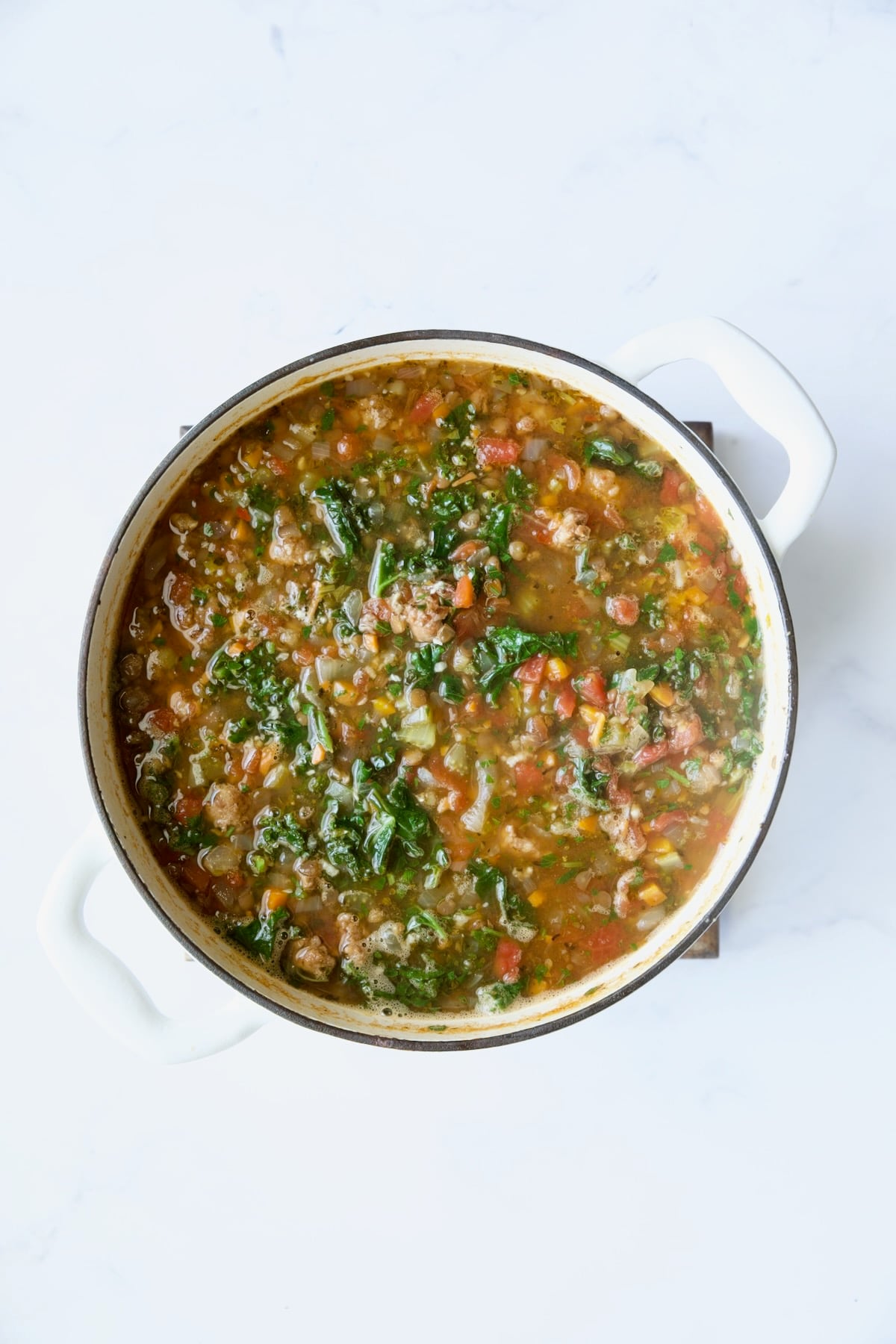 Finished Sausage and Lentil Soup with Kale in white Dutch oven.