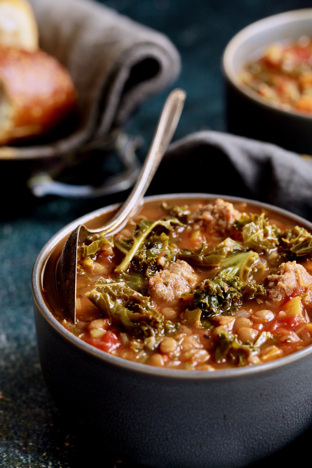 Sausage and Lentil Soup with Kale in gray bowl with spoon resting on the edge.