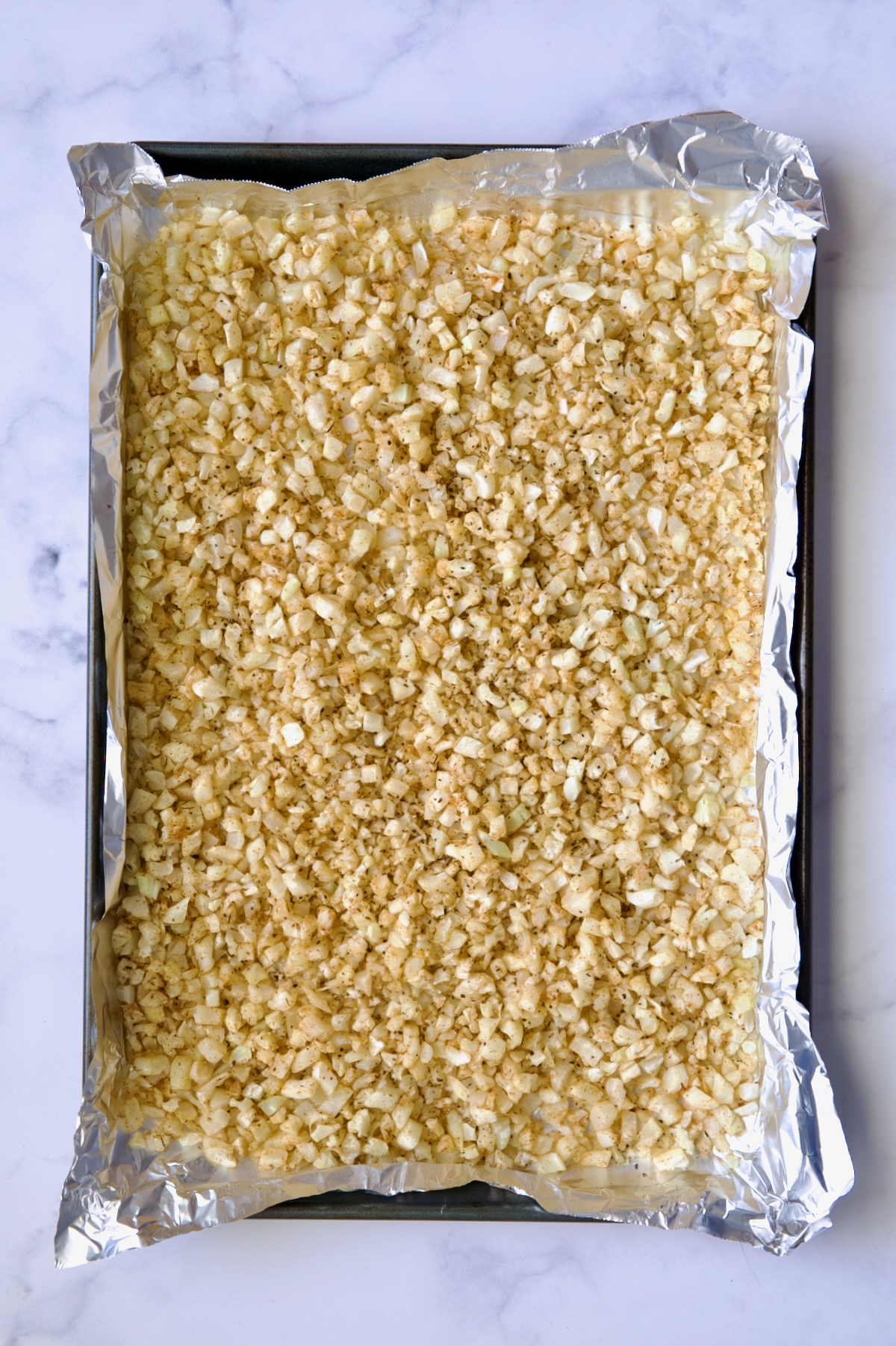 Cooked riced cauliflower on a sheet pan lined with aluminum foil.