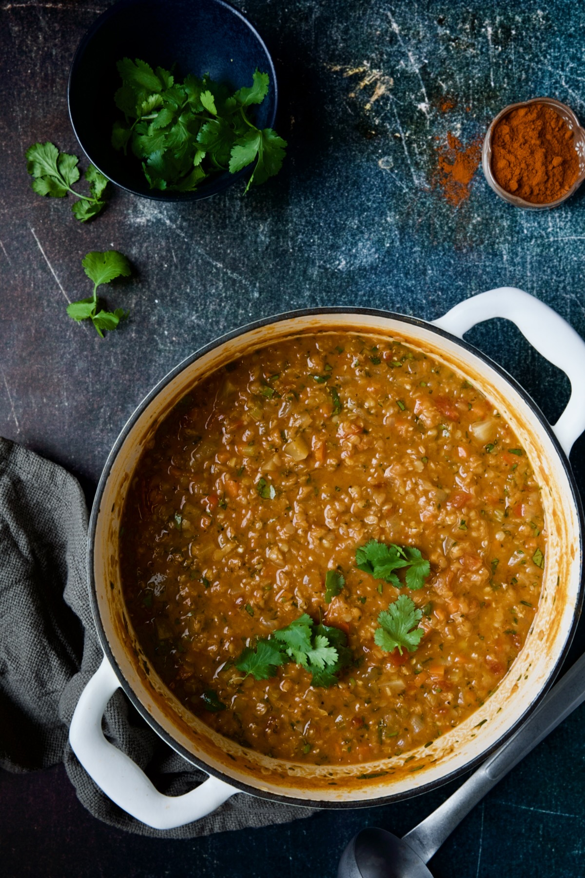 Ethiopian Red Lentil Vegetable Soup in white Dutch oven with bowl of cilantro and berbere spice.