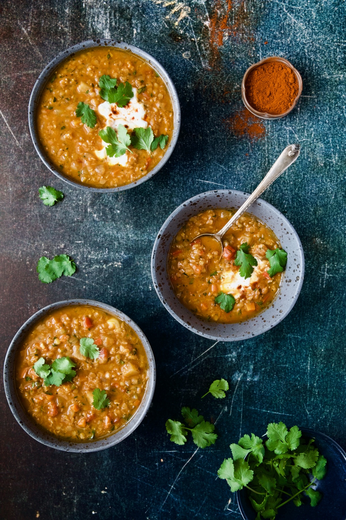 Three bowls of Ethiopian Red Lentil Vegetable Soup on blue distressed background.