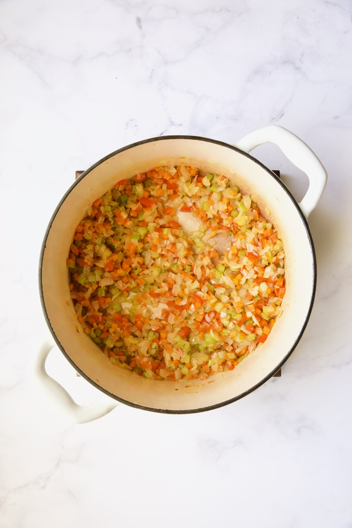 Cooked onions, carrots and celery in white Dutch oven.