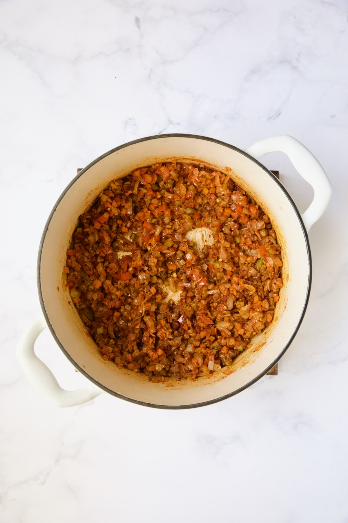 Sauteed vegetables and berbere spice in white Dutch oven.